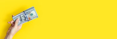 Sarı arka planda izole edilmiş bir yığın banknotla el ele tutuşuyoruz. Zenginlik ya da kredi konsepti. Kopyalama alanı olan uzun Pankart