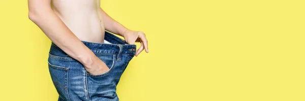 Konzept der Ernährung, richtige Ernährung, Gewichtsverlust Schlanke Frau zeigt lose Jeans und ihr Gewicht zu verlieren. Frau in Oversize-Jeans isoliert auf gelbem Hintergrund. Banner mit Kopierraum — Stockfoto