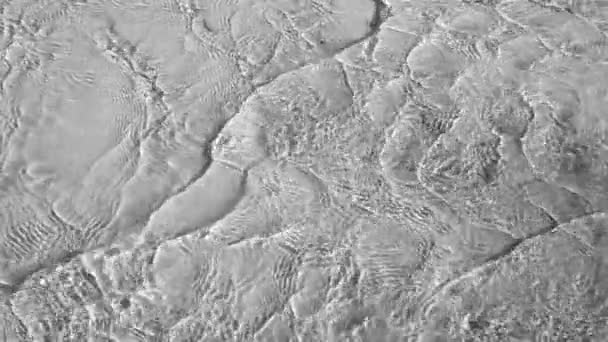 Hermosa aguas poco profundas fluye con reflejos solares La superficie de un río transparente brillante o textura de agua de mar con círculos y ondulaciones en el agua Cámara lenta full HD video en blanco y negro — Vídeos de Stock