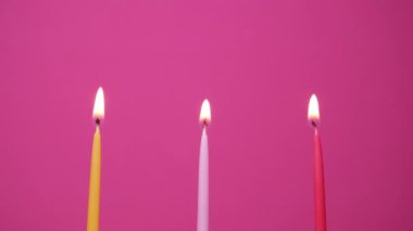 Pembe arka planda yanan üç pasta mumu. Sarı, pembe ve morumsu pasta mumlarını yakın. 4K çözünürlük videosu
