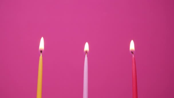 Drie taart kaarsen branden op een roze achtergrond. Sluit af met gele, roze en magenta taart kaarsen. 4K resolutie video — Stockvideo