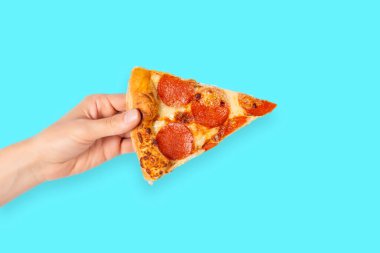 Elinde bir dilim pepperoni pizza, mavi üzerine izole edilmiş. Kağıtlı pizzanın en üst görüntüsü. İtalyan yemeği, sokak yemeği, fast food, fast food..