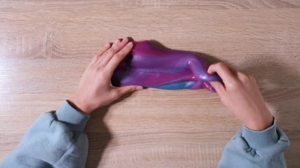 Bermain dengan lendir, meregangkan zat lengket untuk bersenang-senang dan menghilangkan stres. Close up and top view of female hand holding blue, pink and purple shining slime and squeezing it. Video 4K — Stok Video