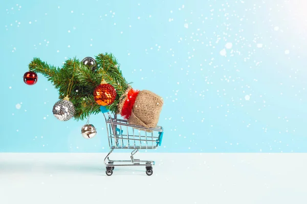 Julgran dekorerad med juldekorationer i en kundvagn från snabbköpet isolerad på blå bakgrund med fallande snö. Nyår eller jul försäljning koncept. Banner med kopieringsutrymme. — Stockfoto