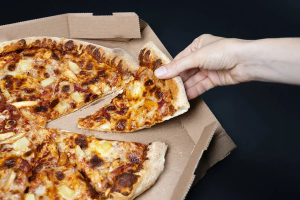 Hand taking a slice of pizza from pizza box. Big Hawaii pizza without one piece. Top view on Hawaii pizza. Concept for italian food, street food, fast food, quick bite
