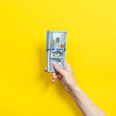 Sarı arka planda izole edilmiş bir yığın banknotla el ele tutuşuyoruz. Zenginlik ya da kredi kavramı