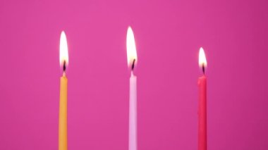 Pembe arka planda yanan üç pasta mumunu üflüyorum. Sarı, pembe ve morumsu kek mumlarını söndürün. Tam HD çözünürlük yavaş çekim mutlu yıllar videosu