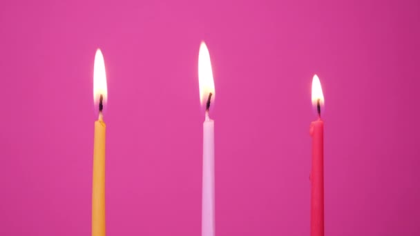 Soufflage de trois bougies à gâteau brûlant sur un fond rose. Gros plan sur souffler des bougies jaunes, roses et magenta gâteau. Résolution Full HD ralenti vidéo joyeux anniversaire — Video