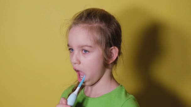 Teenager-Mädchen putzt ihre Zähne isoliert auf leuchtend gelbem Hintergrund. Mädchen im grünen T-Shirt putzt ihre Zähne mit einer elektrischen Zahnbürste — Stockvideo