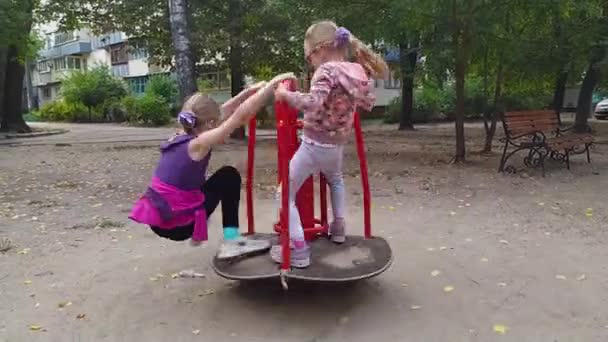 Två tjejer som snurrar på en karusell på en lekplats. Barn som har roligt och leker på lekplatsen — Stockvideo