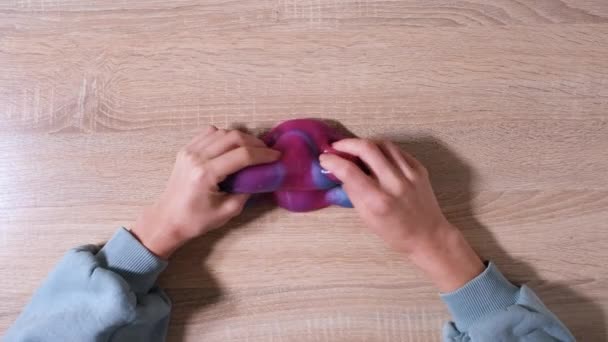 Spelen met slijm, rekken van de kleverige stof voor plezier en stress verlichting. Close-up en bovenaanzicht van vrouwelijke hand die blauw, roze en paars glanzend slijm vasthoudt en knijpt. 4K-video — Stockvideo