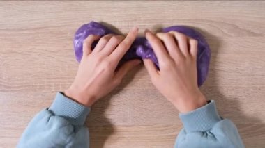 Çamurla oynamak, eğlence ve stres atmak için yapışkan maddeyi germek. Yakın çekim ve üst görüntü, elinde mor parlak balçık tutan ve sıkan kadın eli. 4K video.