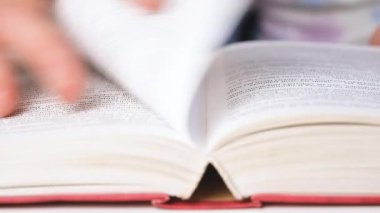 Sayfaların elle çevrildiği açık bir kitabın kapağı. Okumak, çalışmak ya da bilgi aramak. Eğitim ve edebiyat kavramı