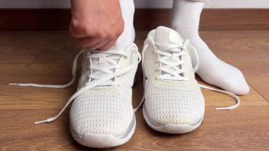 Beyaz spor ayakkabı giyen ve ayakkabı bağcıklarını içeride bağlayan bir kadına yaklaş. Ahşap zeminde spor, koşu, antrenman ya da günlük aktivitelere hazırlanılıyor