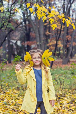 Sarı yağmurluklu küçük güzel kız parkta yürüyor..