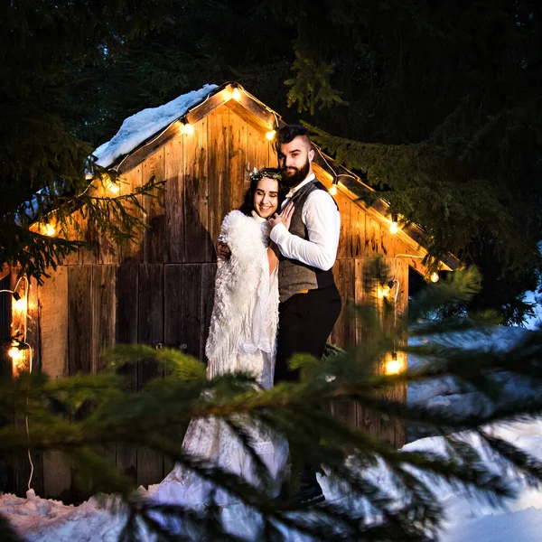 Pareja recién casada, novia y novio en el fondo de una antigua casa de madera y guirnalda retro. Boda rústica de invierno. —  Fotos de Stock