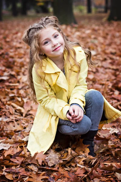 Маленькая красивая девочка в жёлтом плаще гуляет по парку. — стоковое фото