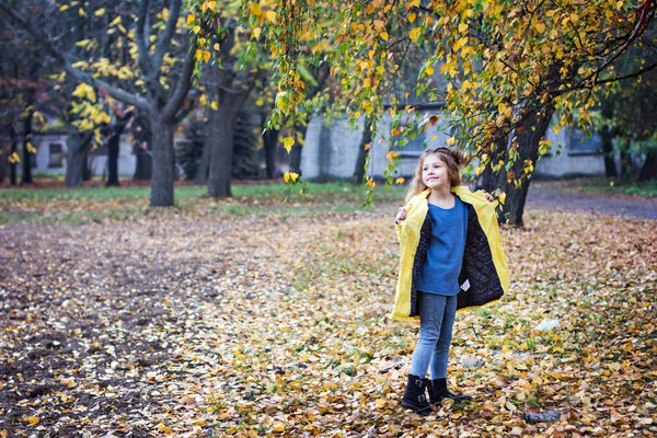 Little beautiful girl in a yellow raincoat walks in the park. — Stock Photo, Image