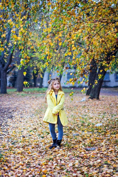Petite belle fille en imperméable jaune se promène dans le parc. — Photo