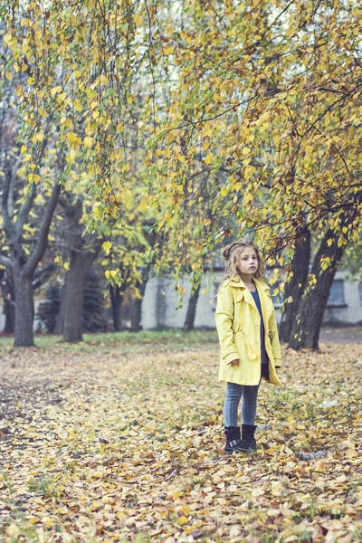 Petite belle fille en imperméable jaune se promène dans le parc. — Photo