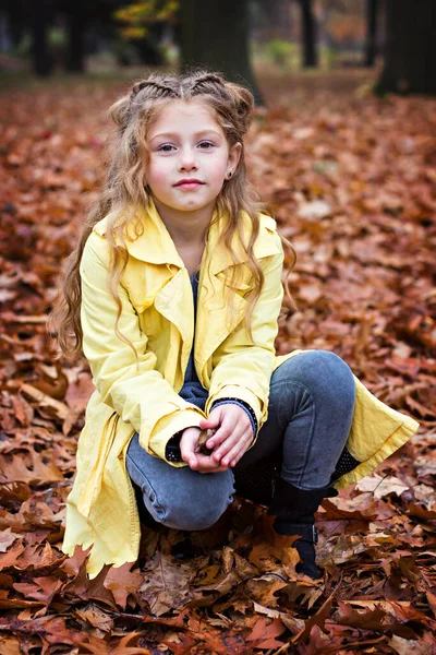Mała piękna dziewczynka w żółtym płaszczu spaceruje po parku. — Zdjęcie stockowe