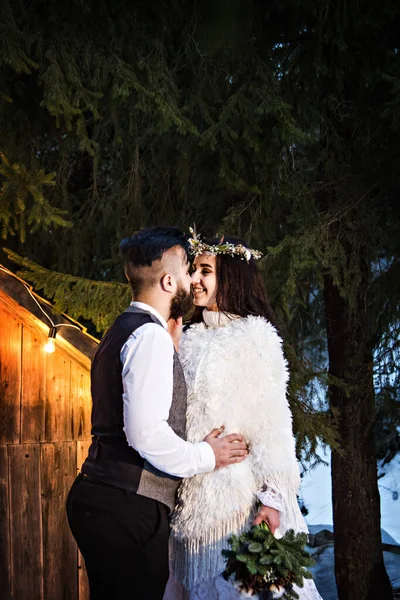 Pareja recién casada, novia y novio en el fondo de una antigua casa de madera y guirnalda retro. Boda rústica de invierno. —  Fotos de Stock