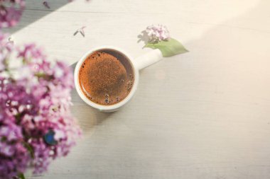 Pencerede bir buket leylak ve güneş ışığında beyaz bir fincanda kahve. Bir buket leylak ve bir fincan kahve veya çay.. 