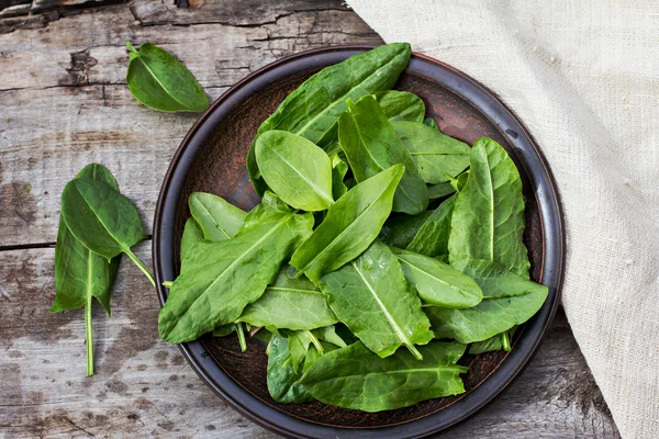 Sorrel leaves on a plate, the plate is on the old boards — Stock Photo, Image