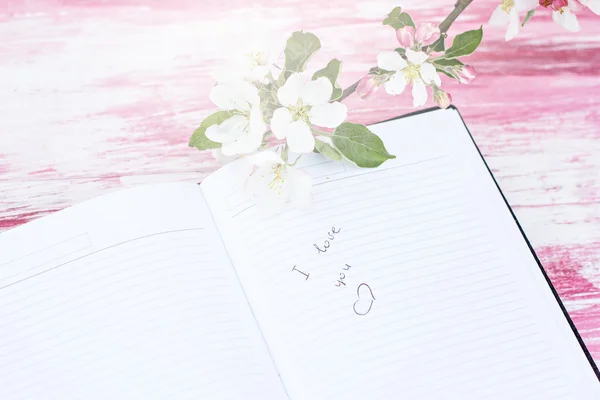 Las ramitas de manzano floreciente con un cuaderno. Escribiendo en un cuaderno, "Te amo " —  Fotos de Stock