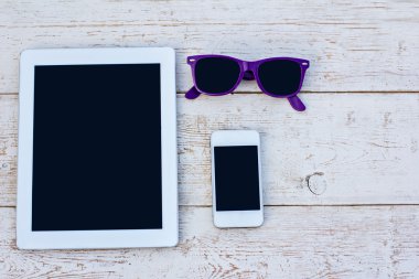 Tablet bilgisayar, cep telefonu ve ahşap bir masa üzerinde güneş gözlüğü