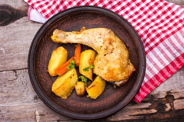 Patates, otlar ve ahşap bir masa üzerinde sarımsak pişmiş tavuk parçaları