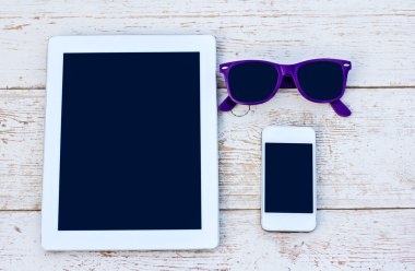 Tablet bilgisayar, cep telefonu ve ahşap bir masa üzerinde güneş gözlüğü