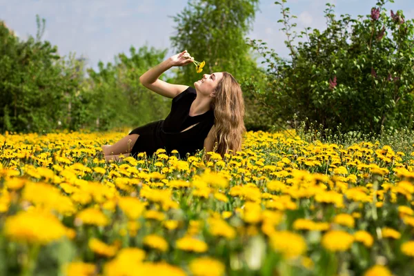 Mulher jovem bonita deitada em um campo, grama verde e flores de dente de leão. Ao ar livre desfrutar da natureza. Menina sorridente saudável deitada na grama verde — Fotografia de Stock