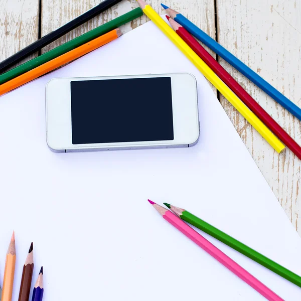 Colored pencils, cell phone and paper on the desk — Stock Photo, Image