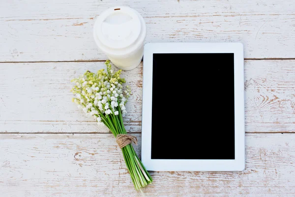 Tablet computer, coffe and  lilies of valley on the table