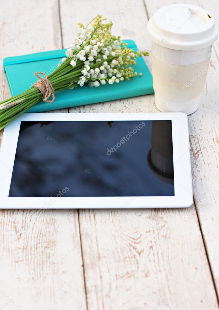 Diary, a tablet computerand  lilies of valley on the table