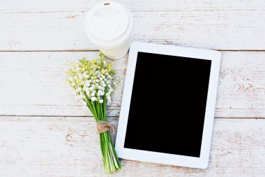 Tablet computer, coffe and  lilies of valley on the table
