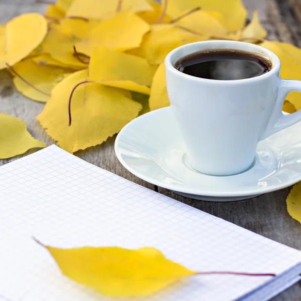 Notebook, xícara de café e folhas de outono amarelas na velha mesa de madeira . Fotografias De Stock Royalty-Free