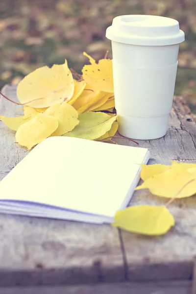 Caderno, xícara de café e folhas de outono amarelas — Fotografia de Stock