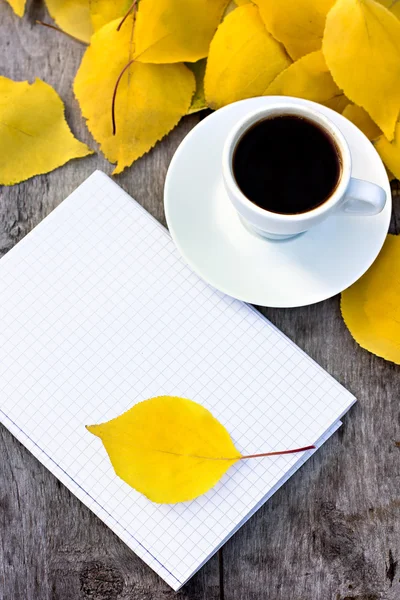 Taccuino, tazza di caffè e foglie autunnali gialle sul vecchio tavolo di legno . — Foto Stock