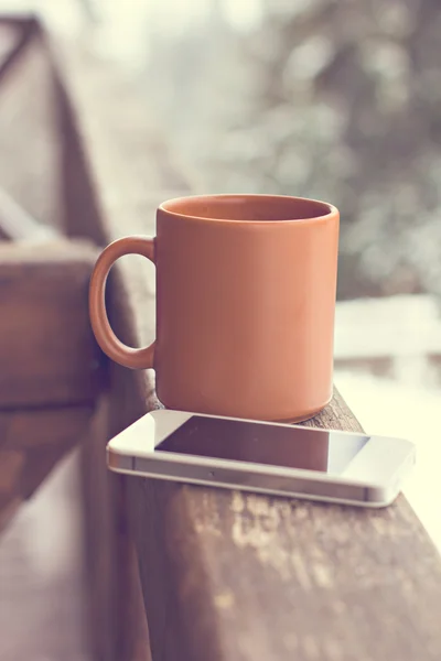 A cup with a hot drink and mobil phone on the background of the winter forest — Stock Photo, Image