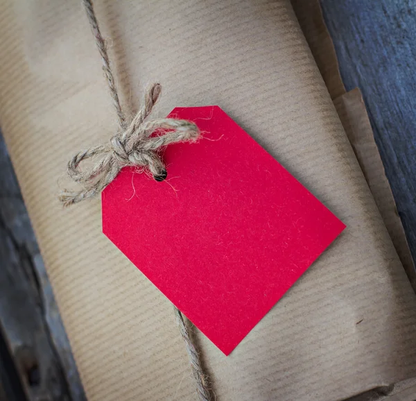 Regalo in carta kraft con cartellino rosso su un tavolo di legno — Foto Stock