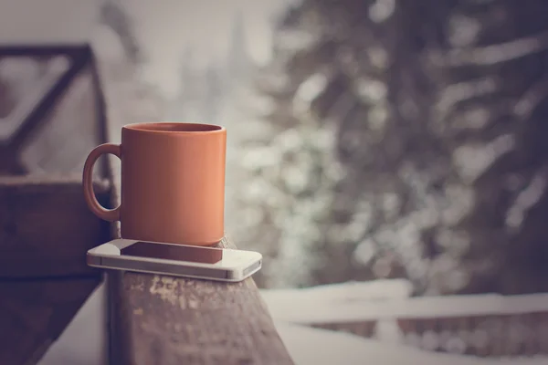 Bir fincan sıcak içecek ve kış orman arka üstünde hareket eden telefon ile