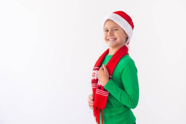 Beyaz arka planda Noel Baba şapkası ve kış eşarbı takan mutlu çocuk portresi. Çocuk Noel zamanı eğleniyor. Mutlu Xmas konsepti