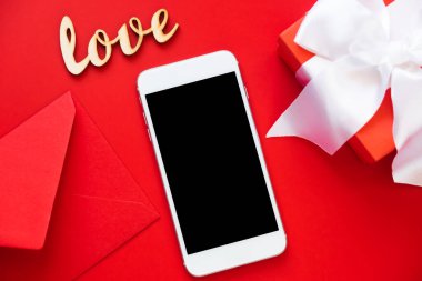 Kırmızı arka planda akıllı telefon, zarf ve hediye kutusu taklidi yap. Sevgililer Günü ya da Anneler Günü için şablon.