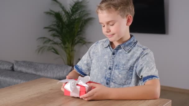 Щасливий хлопчик, який тримає загорнутий подарунок і листівку на День матері або Валентинів. — стокове відео