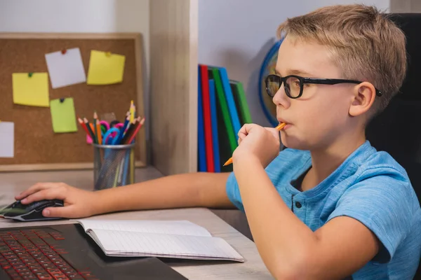 with glasses studies at home while sitting at table in front of laptop. Home learning, online education.