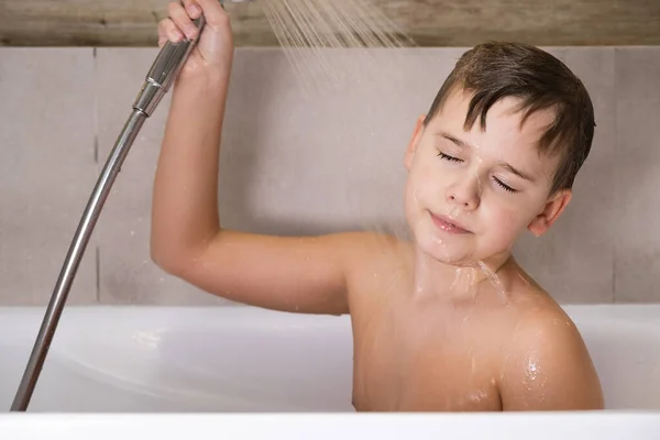 El niño sosteniendo la cabeza de la ducha y se lava la cabeza en el baño infancia saludable — Foto de Stock