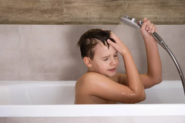 El niño sosteniendo la cabeza de la ducha y se lava la cabeza en el baño infancia saludable — Foto de Stock