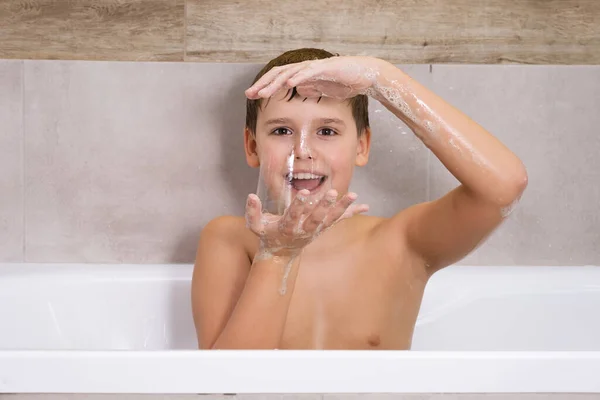Portret chłopca bawiącego się szamponem mydlanym lub żelem w łazience Kąpiel dziecięca i pompuje bańki mydlane — Zdjęcie stockowe
